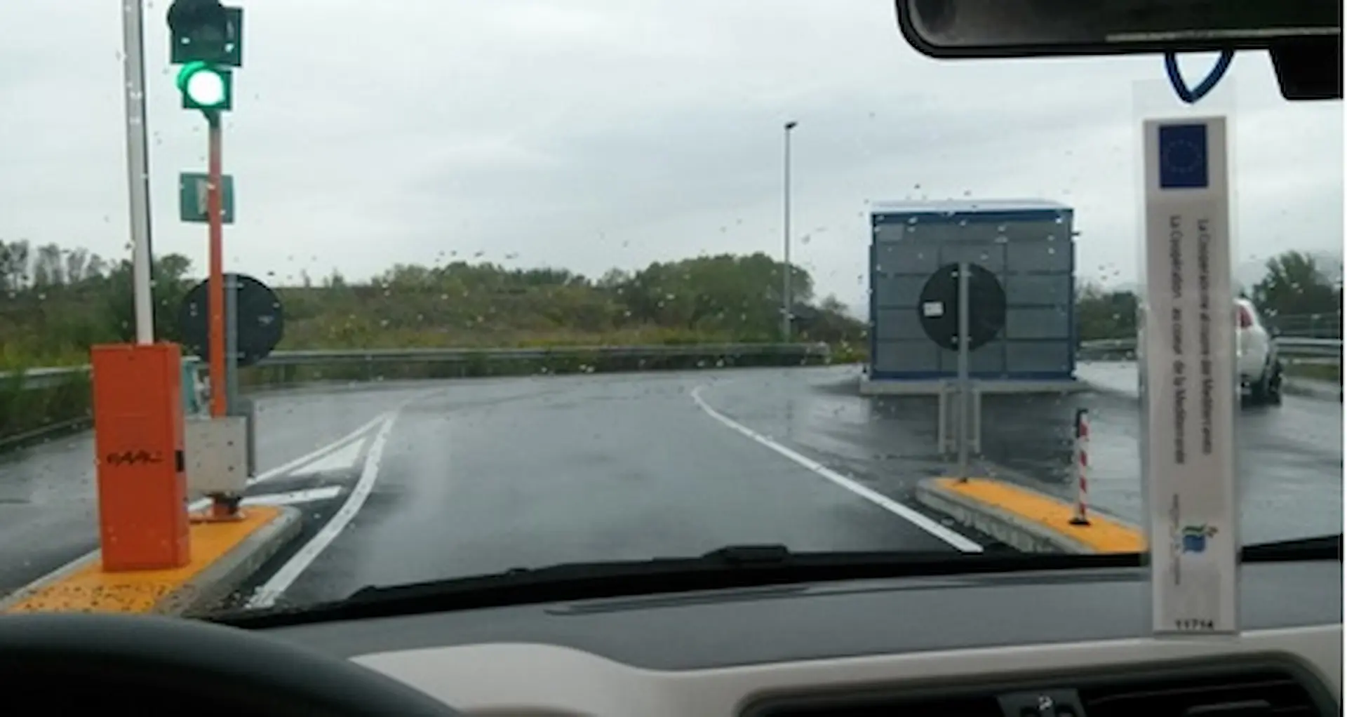 Vista dal veicolo del sistema iTpass, mostrando il tag RFID sul parabrezza e la barriera automatica che si apre al passaggio del veicolo.